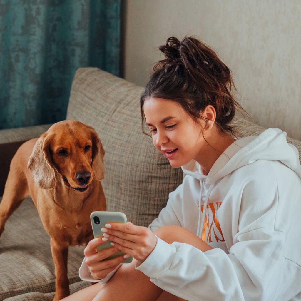 Young woman holding a smartphone in front of a dog